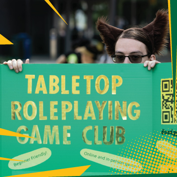 Student in glasses holding up a sign that says "Tabletop Games".